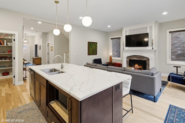 kitchen featuring dark brown cabinetry, sink, a brick fireplace, light hardwood / wood-style flooring, and pendant lighting