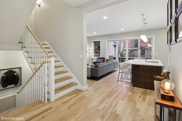 kitchen with sink, a breakfast bar, dark brown cabinets, light hardwood / wood-style floors, and decorative light fixtures