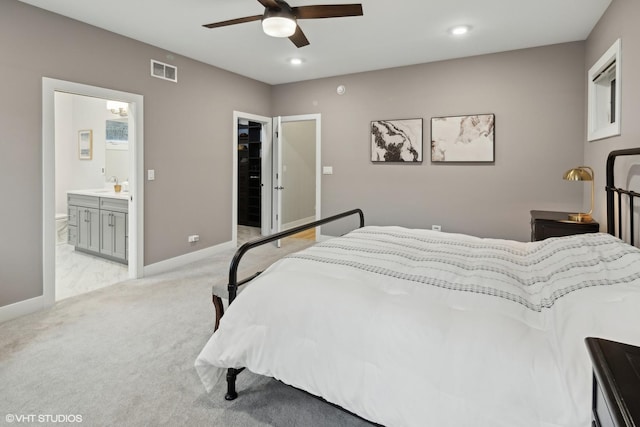 bedroom with connected bathroom, sink, a walk in closet, light colored carpet, and ceiling fan