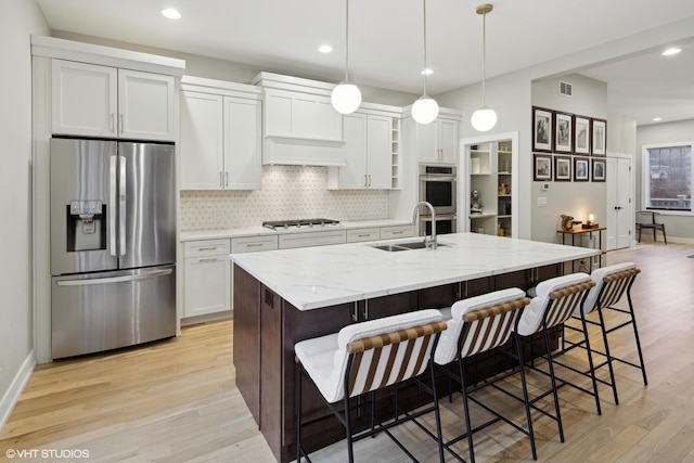 kitchen with sink, white cabinetry, stainless steel appliances, light stone counters, and a center island with sink