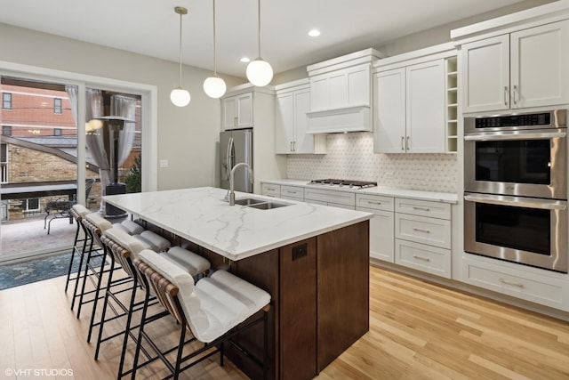 kitchen with sink, appliances with stainless steel finishes, light stone counters, an island with sink, and a kitchen bar