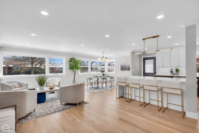 living room with light wood-style floors, recessed lighting, a notable chandelier, and ornamental molding