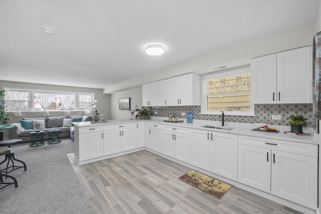 kitchen with sink, white cabinetry, light hardwood / wood-style flooring, kitchen peninsula, and decorative backsplash