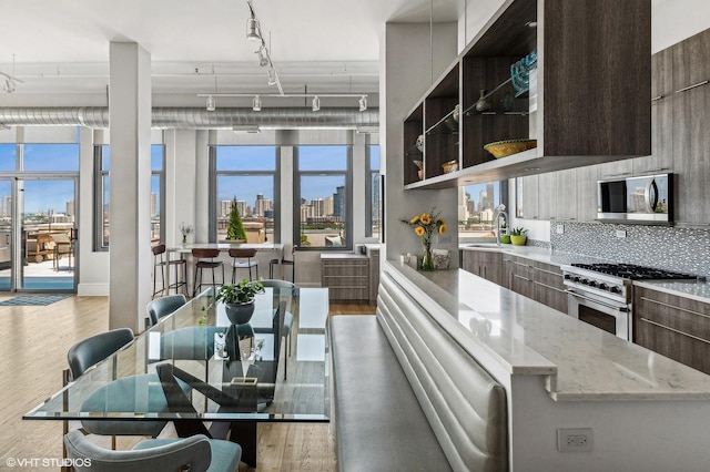 kitchen with sink, stainless steel appliances, light stone countertops, dark brown cabinets, and light hardwood / wood-style flooring