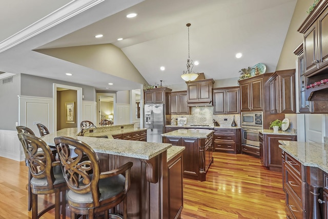 kitchen featuring a breakfast bar area, light stone counters, decorative light fixtures, appliances with stainless steel finishes, and a large island