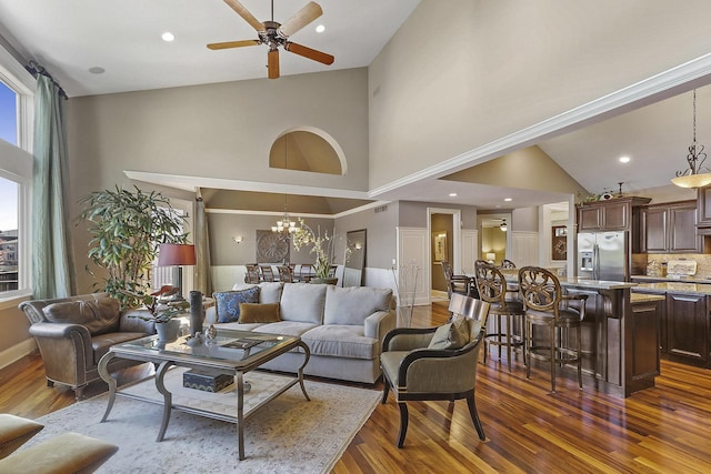 living room featuring dark hardwood / wood-style flooring, ceiling fan with notable chandelier, and a high ceiling