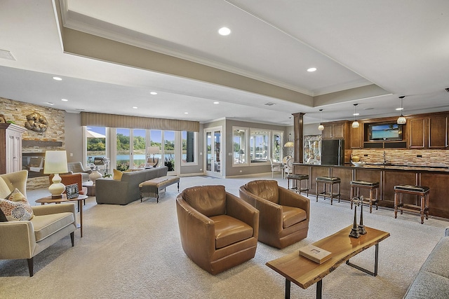 carpeted living room with ornamental molding, plenty of natural light, decorative columns, and a raised ceiling