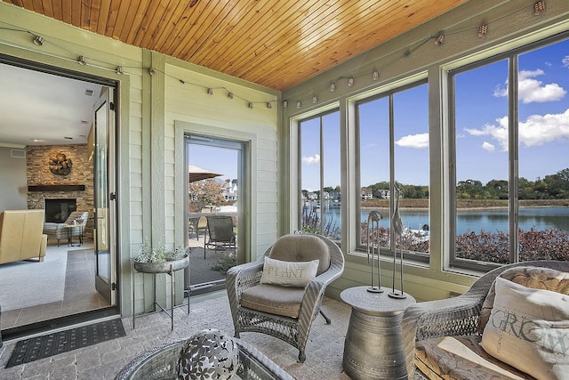 sunroom / solarium with a water view, wooden ceiling, and a stone fireplace