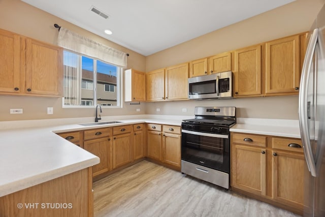 kitchen with stainless steel appliances, sink, and light hardwood / wood-style flooring