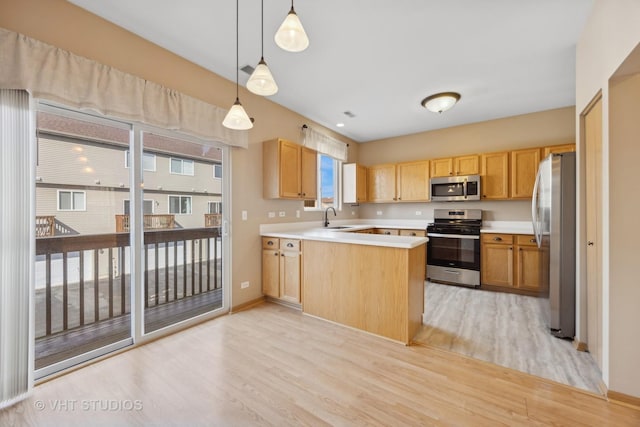 kitchen featuring appliances with stainless steel finishes, decorative light fixtures, sink, kitchen peninsula, and light wood-type flooring