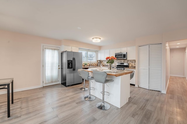 kitchen with a center island, light hardwood / wood-style flooring, a kitchen breakfast bar, stainless steel appliances, and white cabinets