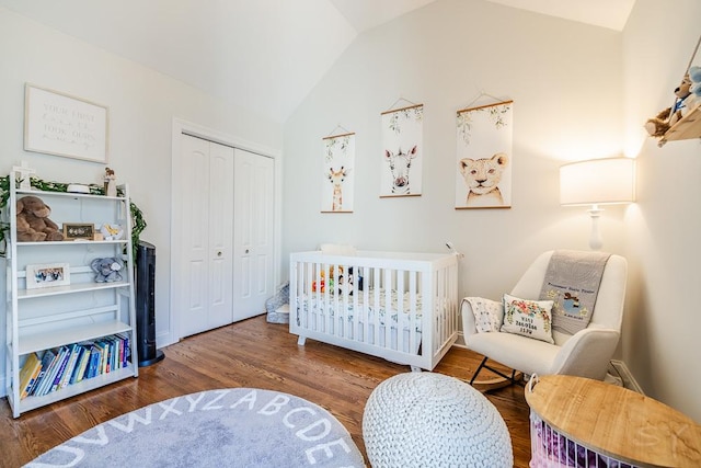 bedroom with lofted ceiling, hardwood / wood-style floors, a crib, and a closet