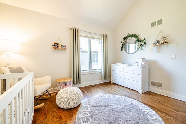 bedroom with wood-type flooring, vaulted ceiling, and a crib