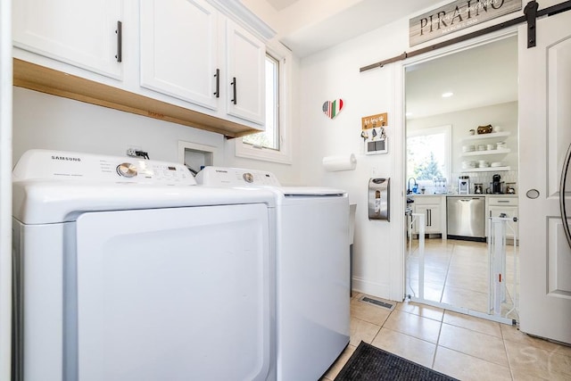 clothes washing area with cabinets, a barn door, washer and dryer, and light tile patterned floors