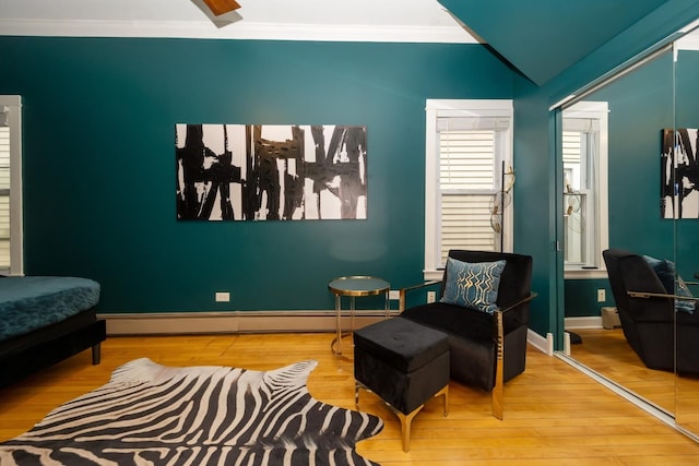 living area with lofted ceiling, hardwood / wood-style floors, ornamental molding, and a baseboard heating unit