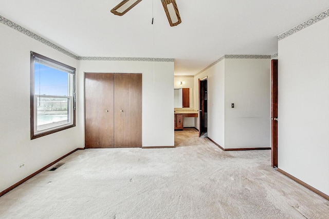 unfurnished bedroom featuring ceiling fan, light colored carpet, ensuite bath, and a closet