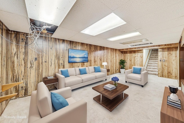 living room with carpet flooring, a drop ceiling, and wood walls