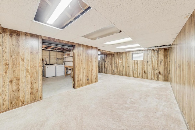 basement with a drop ceiling, carpet floors, independent washer and dryer, and wood walls