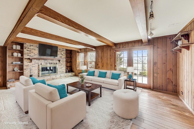 living room featuring beam ceiling, light hardwood / wood-style flooring, a fireplace, and wood walls