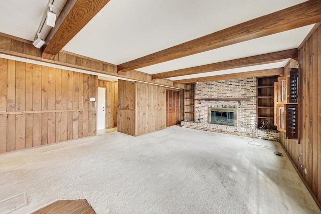 unfurnished living room featuring a fireplace, wood walls, beamed ceiling, carpet floors, and built in shelves