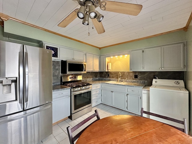 kitchen with sink, tasteful backsplash, light tile patterned floors, appliances with stainless steel finishes, and washer / clothes dryer