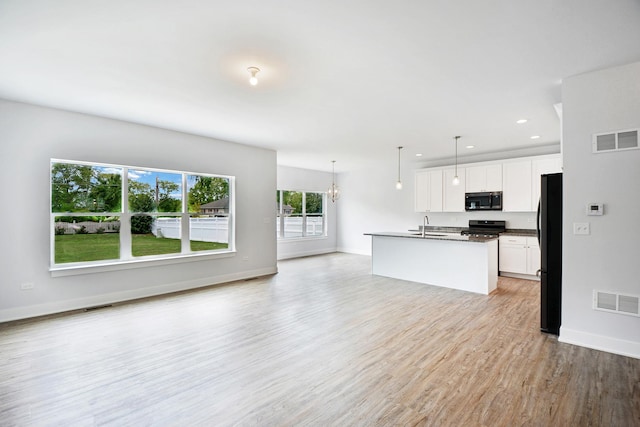 kitchen featuring pendant lighting, white cabinetry, an island with sink, stove, and black fridge