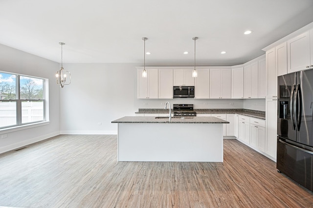 kitchen with white cabinetry, appliances with stainless steel finishes, decorative light fixtures, and a kitchen island with sink