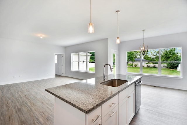 kitchen with an island with sink, sink, white cabinets, light stone counters, and light hardwood / wood-style flooring