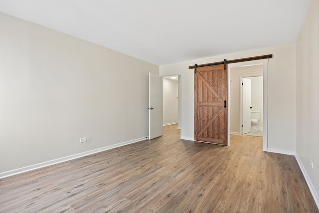 unfurnished bedroom with ensuite bath, light hardwood / wood-style floors, and a barn door