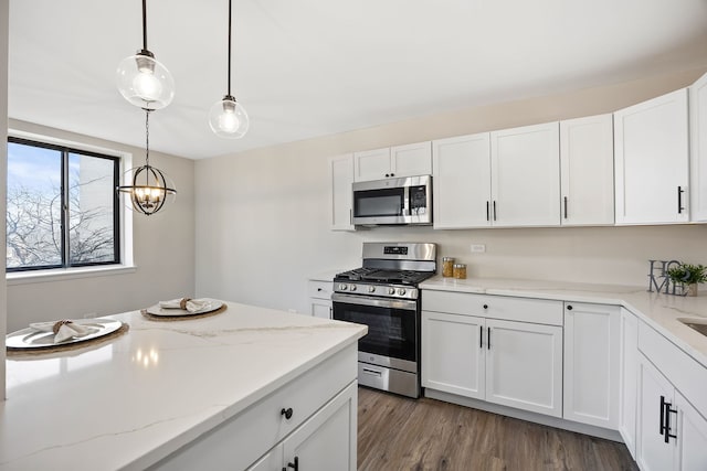 kitchen featuring light stone counters, dark hardwood / wood-style floors, pendant lighting, stainless steel appliances, and white cabinets