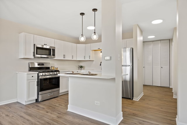 kitchen featuring pendant lighting, light hardwood / wood-style floors, white cabinets, and appliances with stainless steel finishes