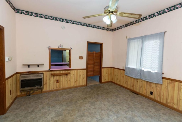 unfurnished living room with ceiling fan, heating unit, and wood walls