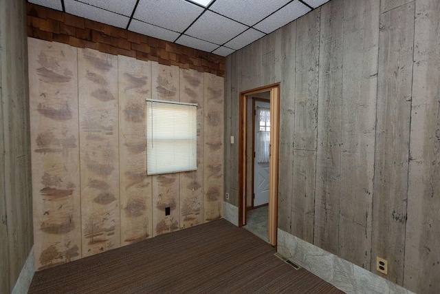 carpeted spare room featuring a paneled ceiling and wood walls