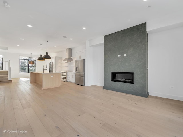 kitchen featuring white cabinetry, pendant lighting, stainless steel appliances, a kitchen island with sink, and wall chimney range hood