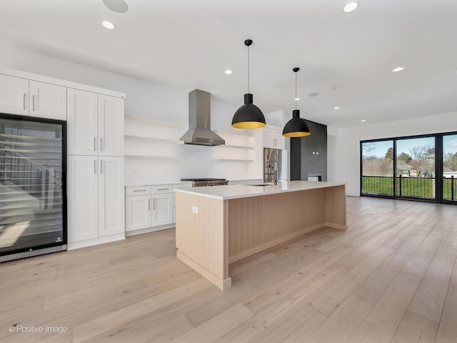 kitchen featuring ventilation hood, white cabinets, decorative light fixtures, a large island with sink, and light wood-type flooring