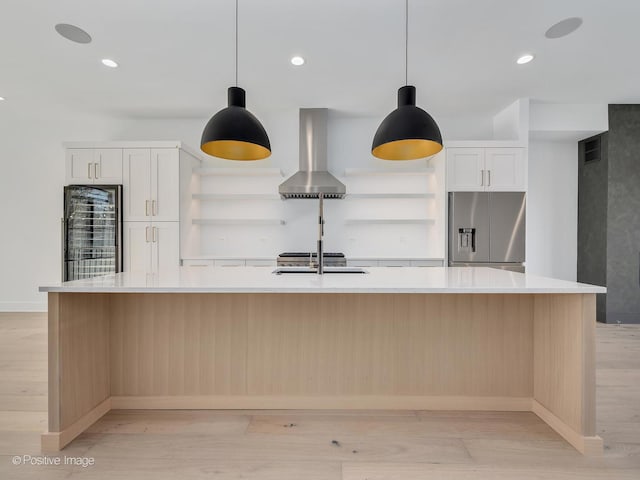 kitchen with stainless steel refrigerator with ice dispenser, wall chimney range hood, a large island, and white cabinets