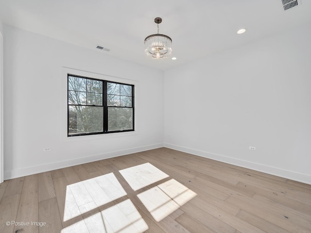 spare room with a notable chandelier and light hardwood / wood-style flooring