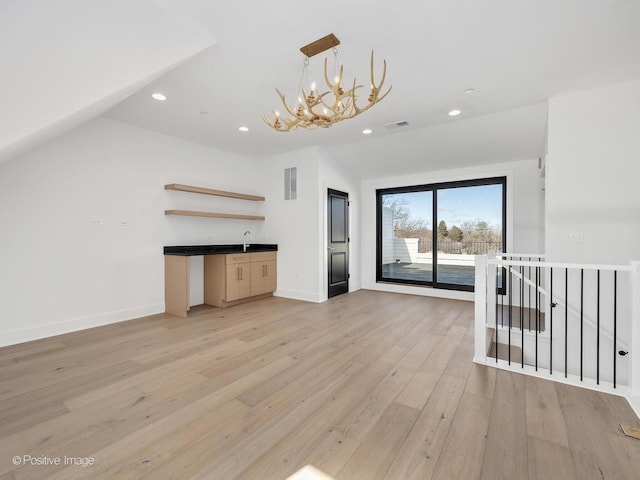 unfurnished living room with sink, vaulted ceiling, a chandelier, and light wood-type flooring