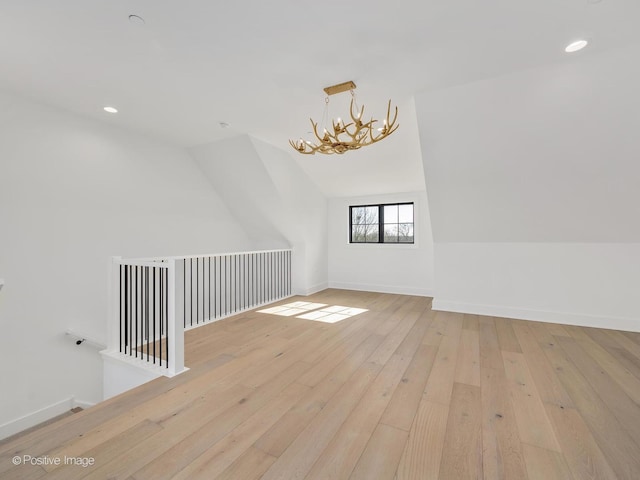 bonus room with a notable chandelier, vaulted ceiling, and light wood-type flooring