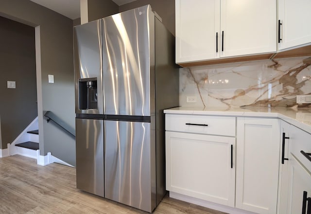 kitchen featuring stainless steel fridge, light stone countertops, white cabinets, decorative backsplash, and light wood-type flooring