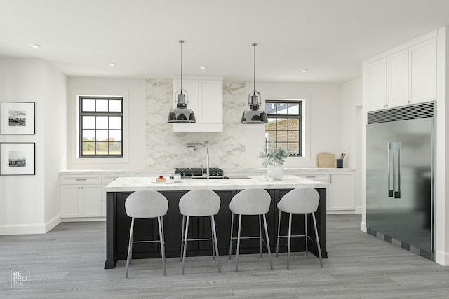 kitchen with decorative light fixtures, white cabinetry, stainless steel built in refrigerator, decorative backsplash, and a kitchen island with sink