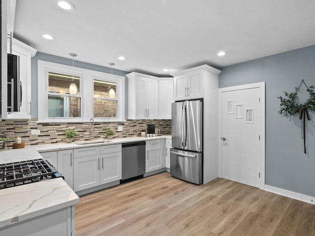 kitchen featuring sink, hanging light fixtures, appliances with stainless steel finishes, light hardwood / wood-style floors, and white cabinets