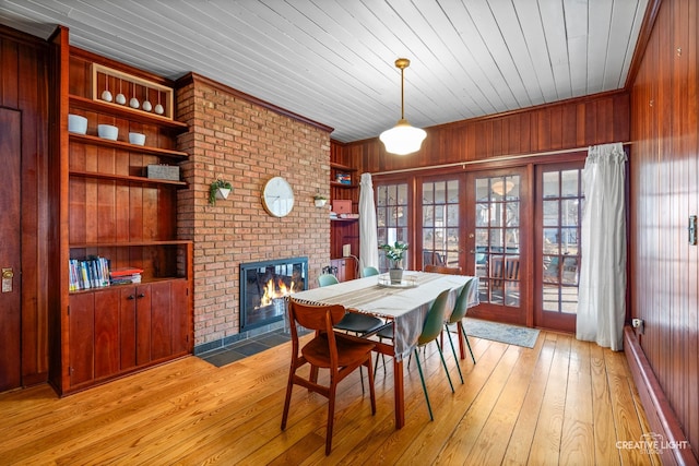 dining room featuring french doors, built in shelves, wood walls, a fireplace, and light hardwood / wood-style floors