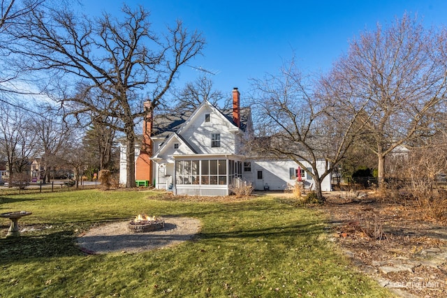 back of property featuring a sunroom, a lawn, and a fire pit