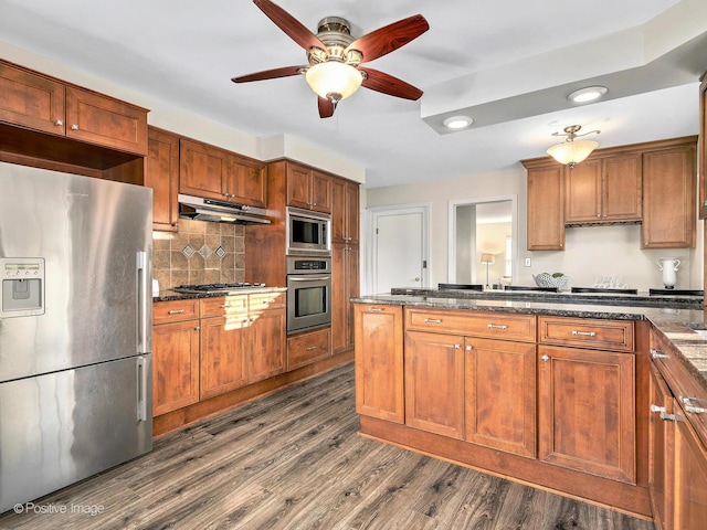 kitchen featuring decorative backsplash, dark wood-style floors, appliances with stainless steel finishes, brown cabinets, and under cabinet range hood