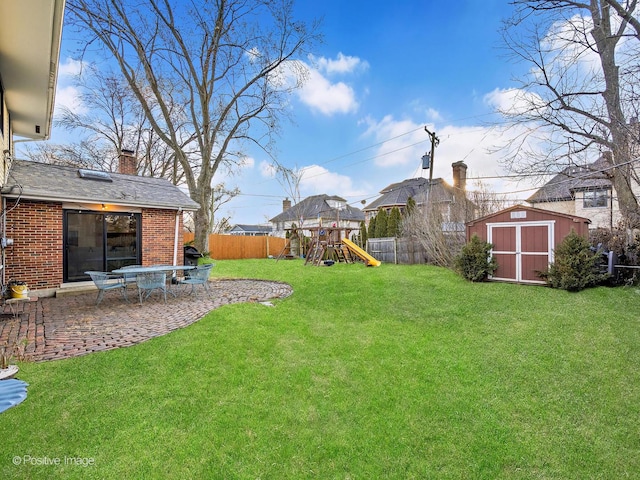 view of yard featuring a playground, a fenced backyard, a storage shed, an outdoor structure, and a patio area