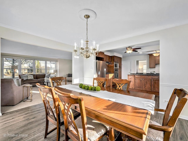 dining room with ceiling fan with notable chandelier, baseboards, and wood finished floors