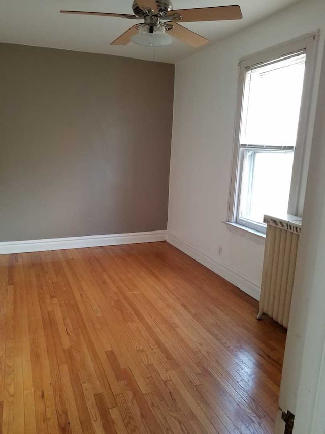 unfurnished room with light wood-style floors, radiator heating unit, baseboards, and ceiling fan