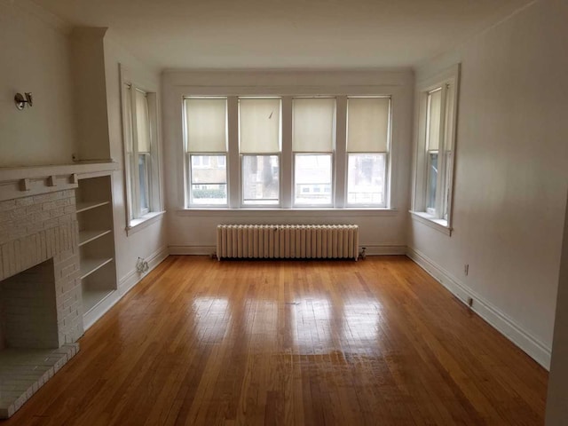 unfurnished living room with radiator, baseboards, plenty of natural light, and hardwood / wood-style floors