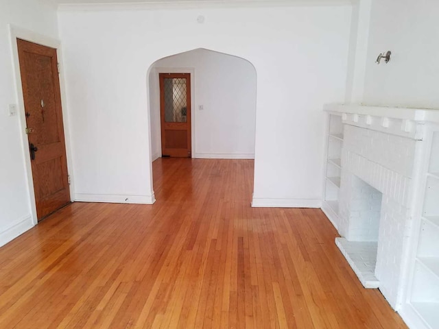 unfurnished living room with light wood-style flooring, a fireplace, arched walkways, and baseboards